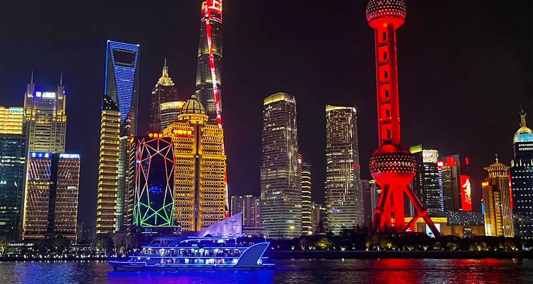 Dazzling night skyline of Shanghai’s Pudong district with brightly lit skyscrapers and a passing cruise boat.