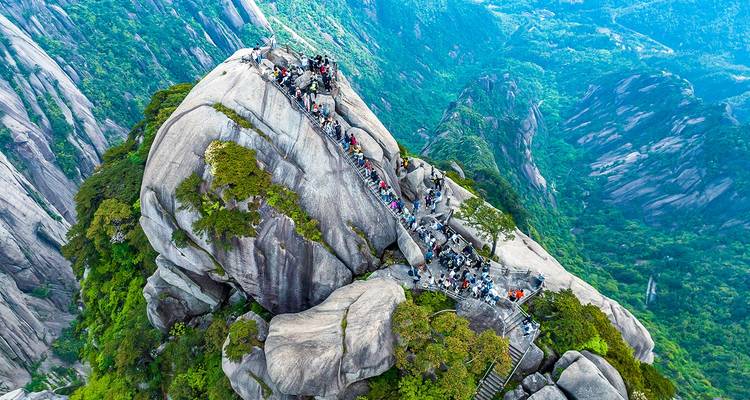 Tientallen wandelaars beklimmen een steile stenen trappenhuizen bovenop een torenhoge granieten spits in het weelderige Huangshan-landschap.