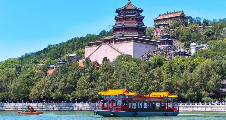 Farbenfrohe Vergnügungsbootfahrten auf einem See neben den kunstvollen Pavillons des Sommerpalasts von Peking, die von bewaldeten Hügeln im Hintergrund umgeben sind.