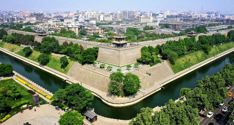 Luftaufnahme des massiven rechteckigen Stadtmauersystems von Xi'an, umgeben von einem Burggraben und der modernen Skyline dahinter.