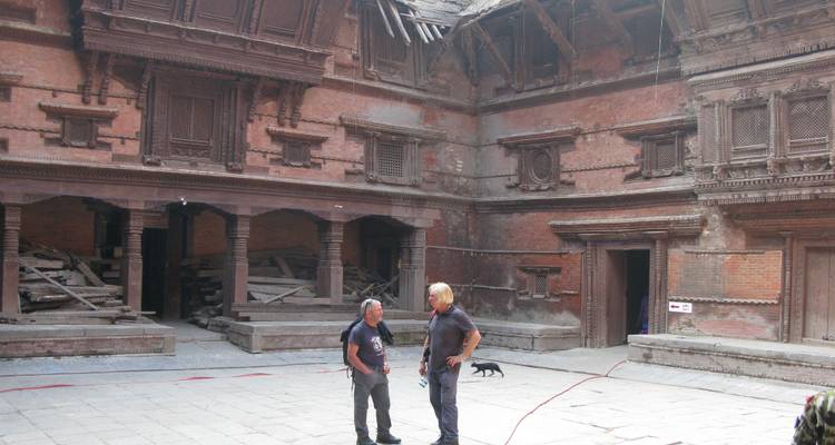 Deux hommes debout dans une cour historique à l'architecture en bois.
