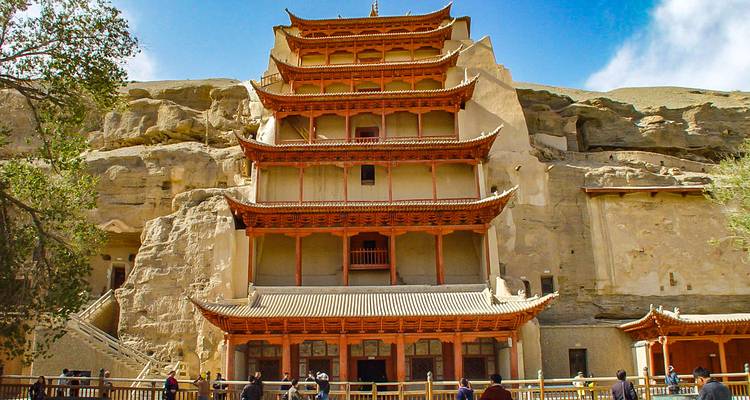 Edificio histórico excavado en un acantilado con turistas.