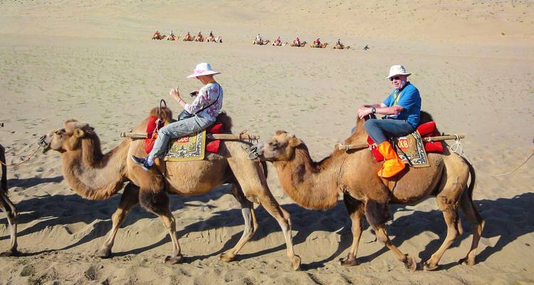 Turistas montando camellos en un entorno desértico.