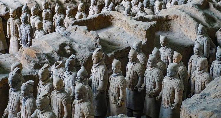 Reihen lebensgroßer Terrakotta-Krieger-Statuen stehen in einer ausgegrabenen Grube mit detaillierten Rüstungen und Gesichtszügen.