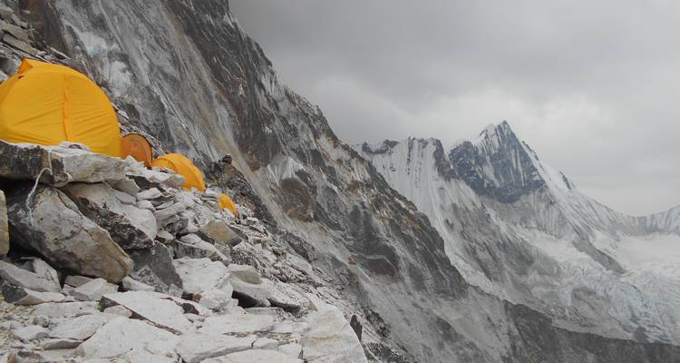 Campsite with yellow tents on rocky slope under overcast sky.