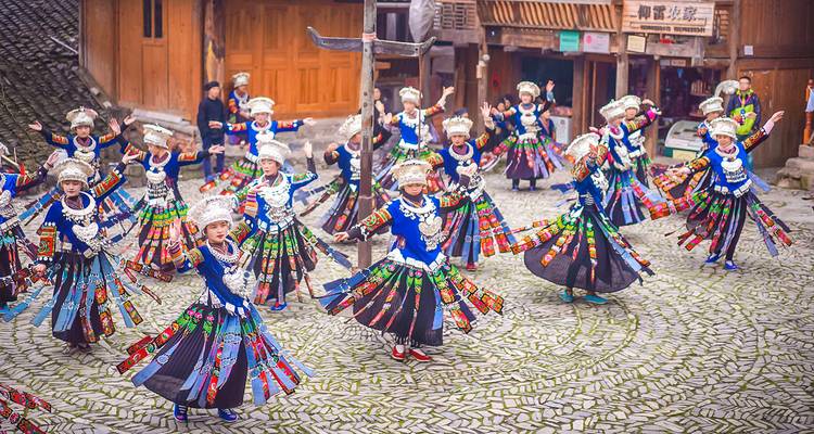 Traditionelle Minderheitstänzer in leuchtenden Kostümen treten auf einem gepflasterten Platz auf.