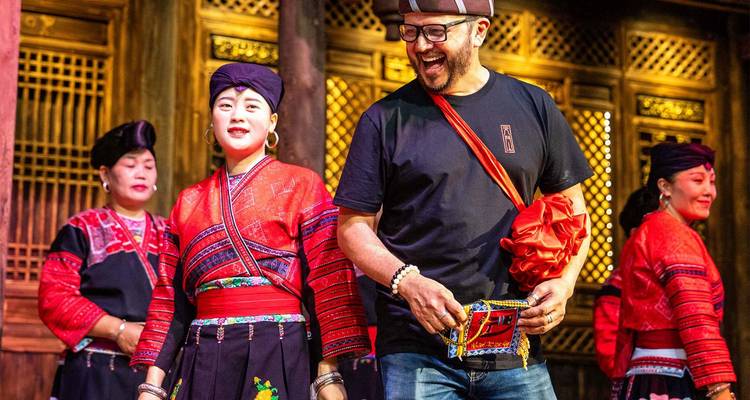 Animada presentación en escena con mujeres Yao o Zhuang en trajes rojos y una turista riendo