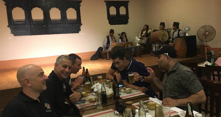 Groupe d'hommes savourant un repas avec de la musique traditionnelle en arrière-plan.