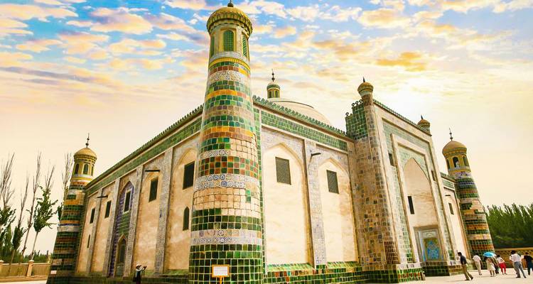 Mezquita ornamentada con minaretes de azulejos al atardecer, rodeada de gente.