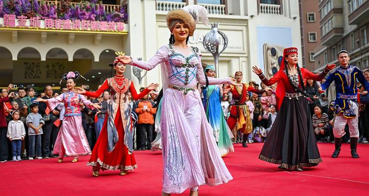 Oeigoerse dansers in kleurrijke traditionele kledij die op een rood tapijt voor een publiek optreden.