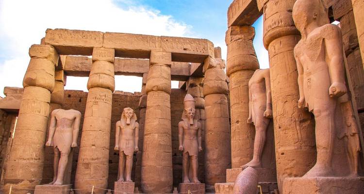 Statues et colonnes d'un temple égyptien antique sous un ciel bleu.