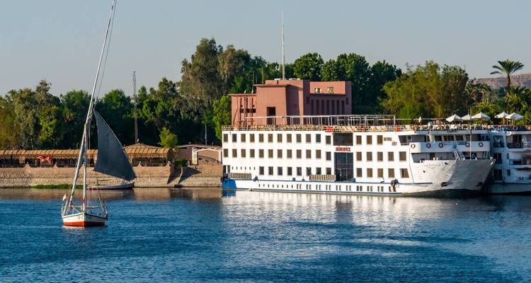 Bateaux sur le fleuve Nil avec un bâtiment et de la verdure en arrière-plan.
