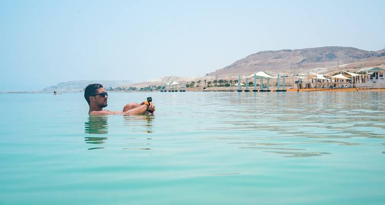Hombre flotando en el Mar Muerto con montañas al fondo.