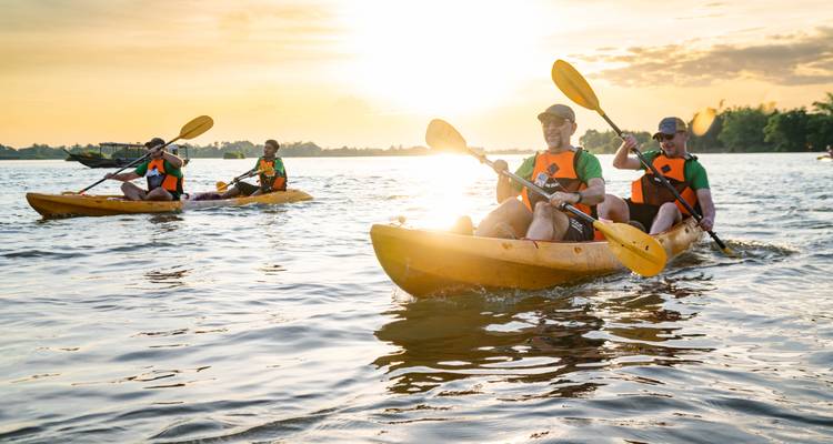 Kayakers paddling at sunset on a smooth body of water.
