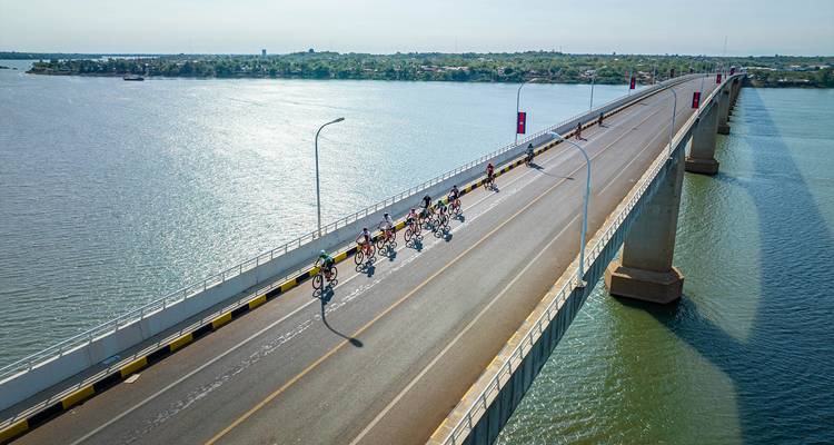 Cyclists riding on a bridge over a large river with a distant view of the city.