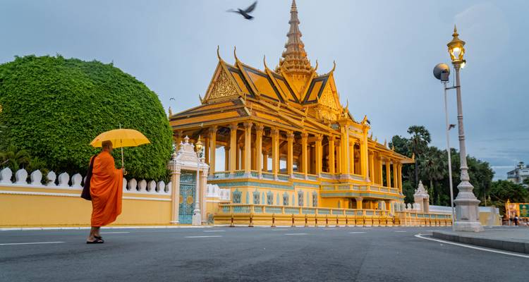 A monk with an umbrella walking past a golden temple complex.