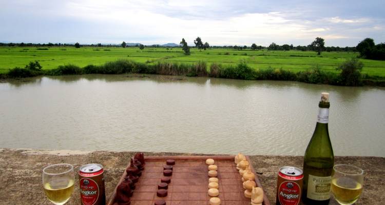 Drinks and chessboard on a table by a calm river.