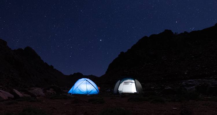Two illuminated tents under a starlit night sky.