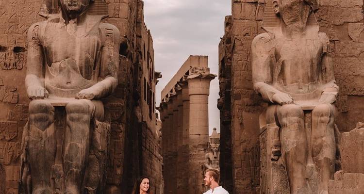 Couple debout entre de grandes statues dans un temple égyptien.
