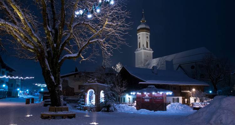 Village enneigé la nuit avec une église éclairée.