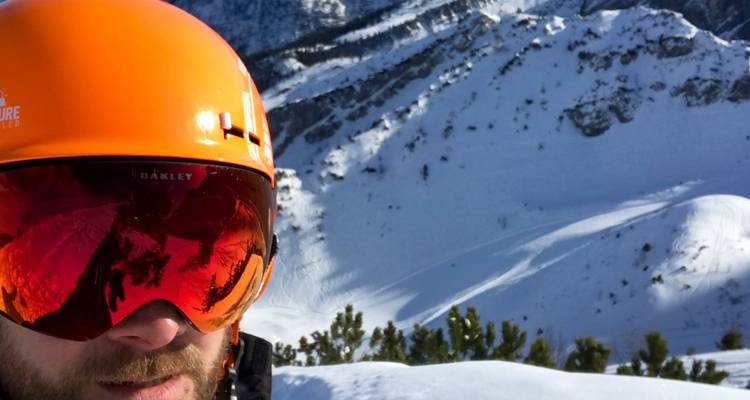 Personne portant un casque de ski avec un paysage de montagne enneigée en arrière-plan.