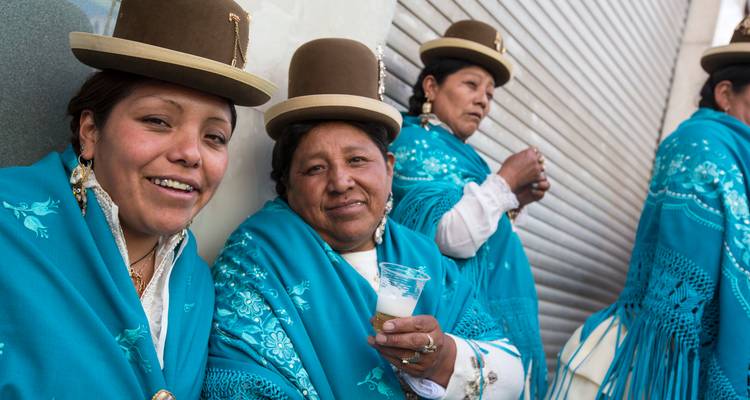 Femmes boliviennes portant des chapeaux melon traditionnels et des châles turquoise, souriantes et buvant dans la rue