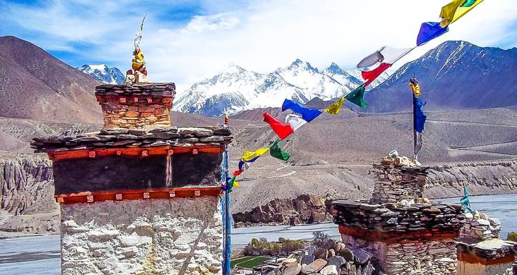 Kloster auf einem Hügel mit bunten Gebetsfahnen und fernen Bergen.