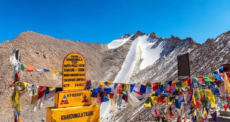 Col de haute montagne avec un panneau panoramique et des drapeaux de prière colorés.