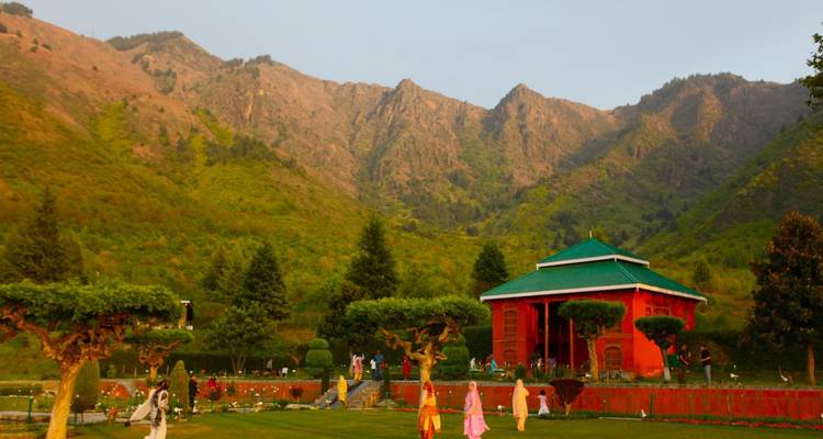 Des personnes se promènent dans un parc avec des montagnes et un pavillon traditionnel.