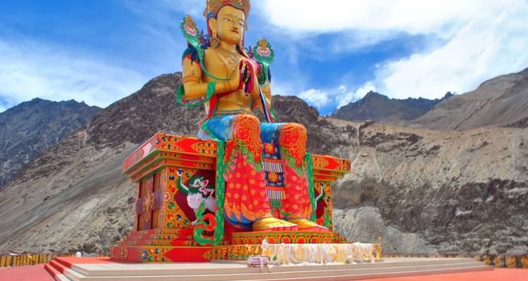Grande statue de Bouddha avec des décorations colorées et des montagnes.