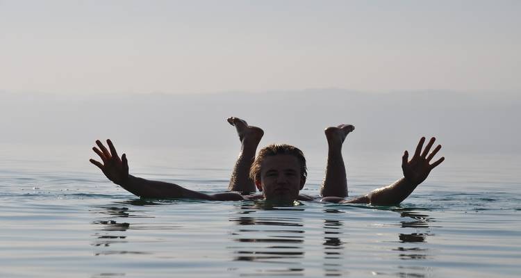 Une personne flottant sur le dos dans une étendue d'eau calme avec un arrière-plan brumeux.