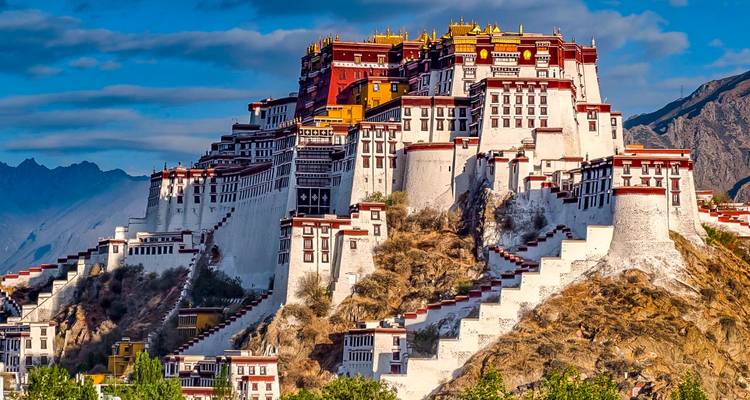 Dramatic view of the multi-tiered white and red Potala Palace perched on a hill against a deep blue sky.