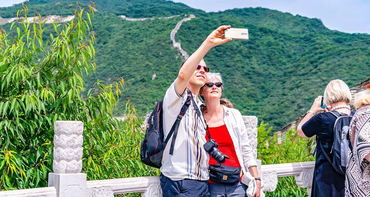 Travellers pause to take a selfie with lush green hills and the winding Great Wall of China in the background.