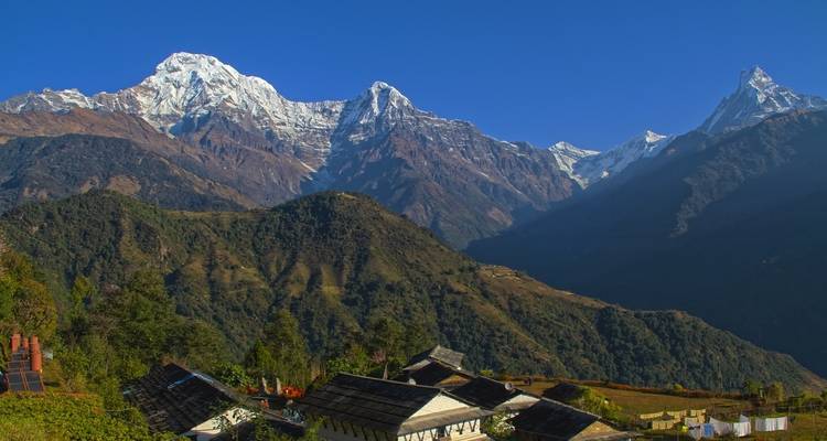 Snow-capped mountains seen from a village in a green valley.