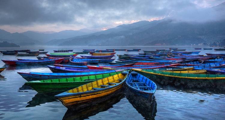 Brightly colored boats on a lake surrounded by misty mountains.