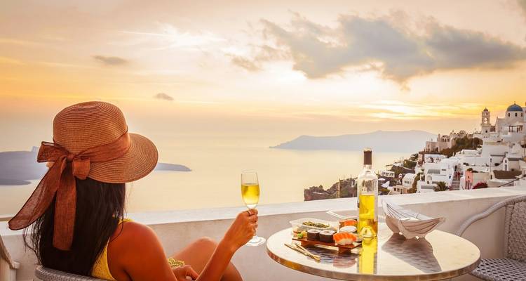 Femme savourant un verre sur une terrasse avec vue sur la mer au coucher du soleil.