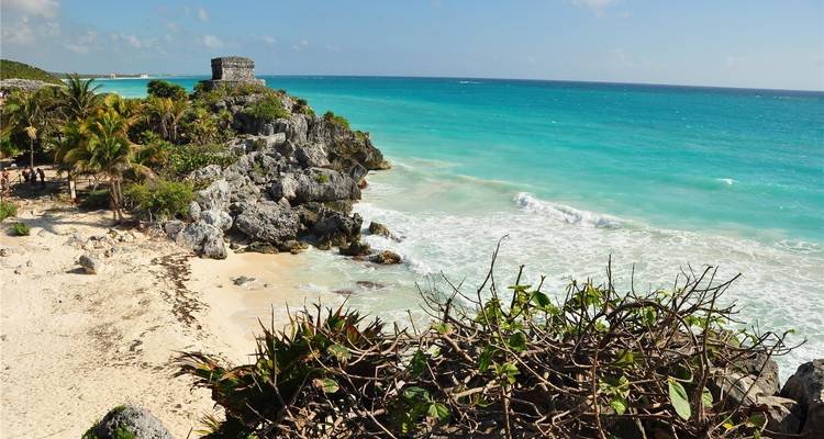 Küstenruinen mit Blick auf ein türkisfarbenes Meer mit Palmen.