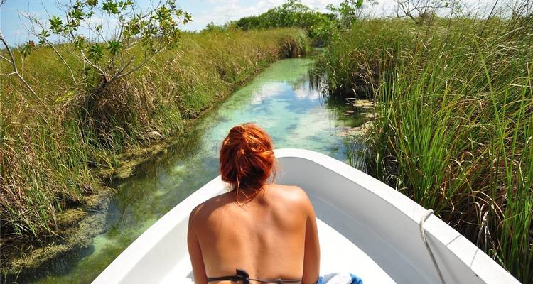 Person, die in einem Boot liegt und durch eine schmale Wasserstraße mit Grünzeug navigiert.