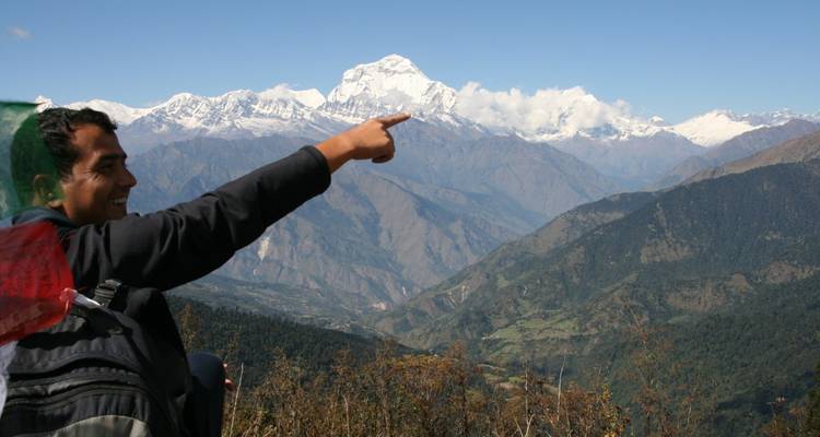 Glimlachende trekker wijst naar een ver weg gelegen, sneeuwbedekte Himalaya-top onder een heldere hemel.