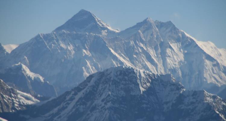 Telefotozicht op de Mount Everest en naburige toppen bedekt met sneeuw tegen een blauwe hemel.