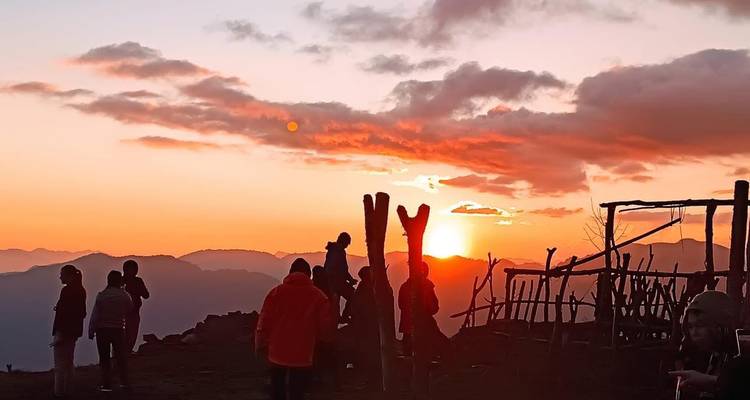 Wandelaars verzamelden zich op een bergrug en keken naar een levendige oranje zonsopgang boven mistige Himalaya-valleien.