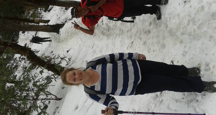 Trekkkers op een smal sneeuwbedekt bospad, waarvan er een naar de camera glimlacht terwijl een ander een vredesteken maakt