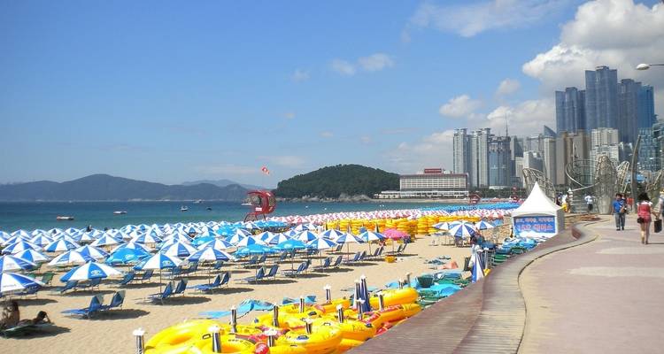 Playa Haeundae en Busán con sombrillas coloridas y edificios de gran altura en el fondo.