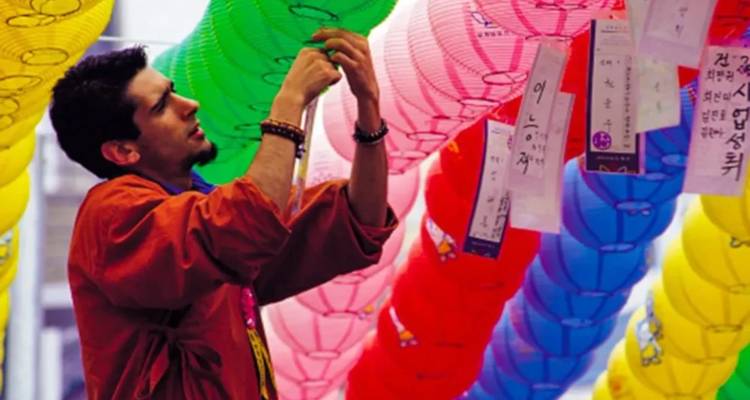 Ein Mann in traditioneller Kleidung haengt bunte Papierlaternern waehrend eines Strassenfestes auf.