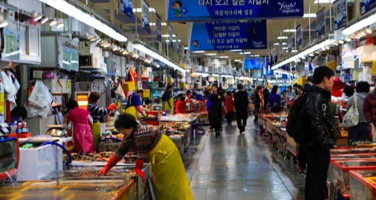Mercado de pescado interior lleno de vida con vendedores y compradores en los pasillos brillantemente iluminados.