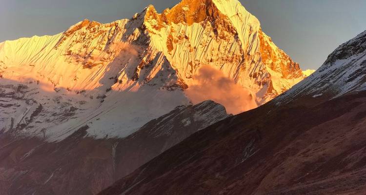 La lueur alpine dorée illumine un pic himalayen dramatique avec de la brume s'échappant de ses parois abruptes.