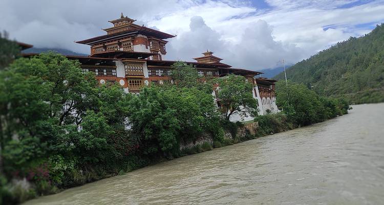 Monasterio-fortaleza bhutanés tradicional encaramado junto a un río con vegetación exuberante y montañas envueltas en niebla.