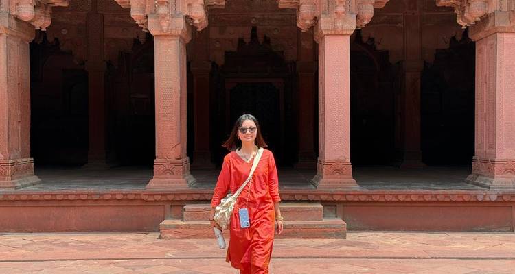 Une femme vêtue d'une robe rouge marche à travers les colonnes en grès ouvragé d'un monument moghol.
