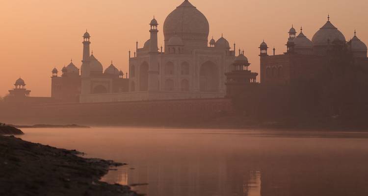 Le Taj Mahal brille doucement dans la brume orange de l'aube au-dessus du fleuve Yamuna.
