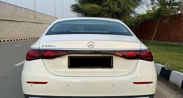 Vue arrière d'une berline Mercedes blanche garée en bordure de route en milieu urbain.